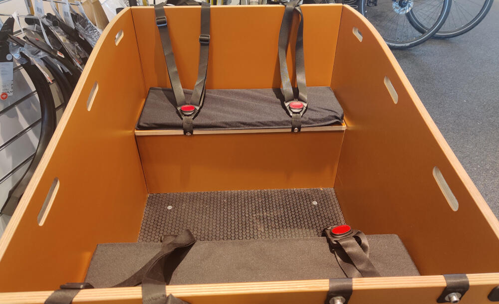 Ladet på en el ladcykel. Ladkassen er lavet af træ og er med polstrede sæder og y-seler til børn.